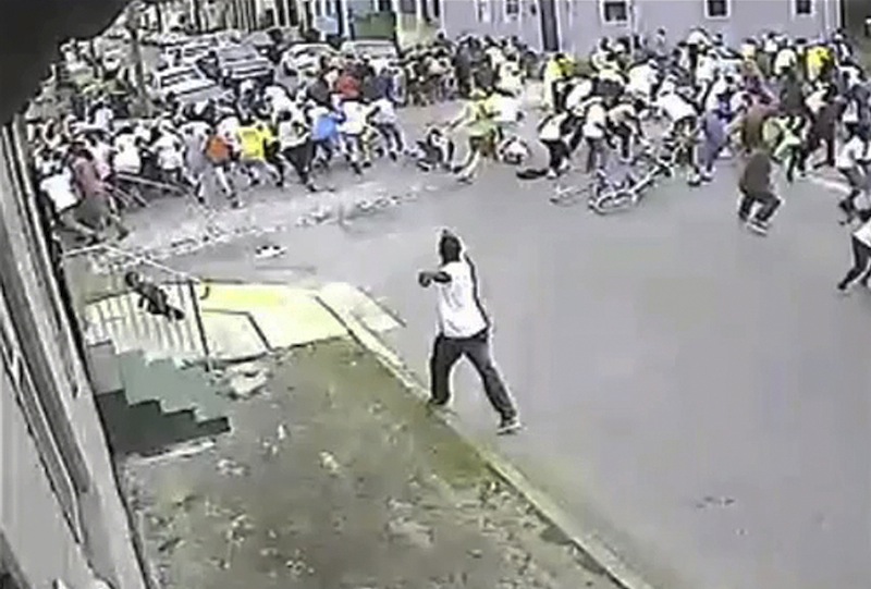 In this image taken from video and provided Monday, May 13, 2013, by the New Orleans Police Department, a possible shooting suspect in a white shirt, bottom center, shoots into a crowd of people, Sunday in New Orleans. The possible suspect may have two accomplices in the Mother's Day gunfire that wounded 19 people during a New Orleans neighborhood parade. (AP Photo/New Orleans Police Department)