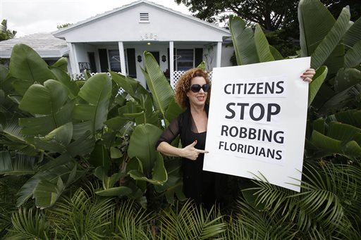 Nancy Loft Powers poses with a sign she made in front of her home in Deerfield Beach, Fla., on Monday. Powers had to sell other properties she owned because she could no longer afford the insurance.