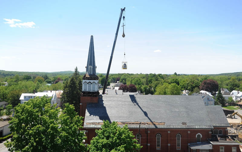 The cross that stood atop the steeple of Saint Francis de Sales Catholic church is hoisted over the church as the steeple is removed by sections during demolition on Tuesday.
