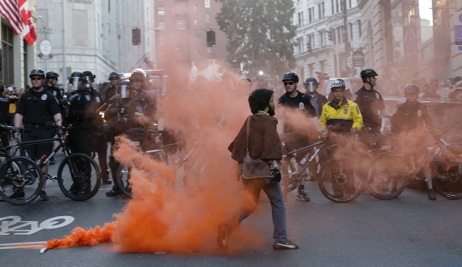 A protester walks away after placing a smoke device on the ground in front of police officers during a May Day march that began as an anti-capitalism protest and turned into demonstrators clashing with police lies on the ground next to police batons, Wednesday, May 1, 2013, in downtown Seattle. (AP Photo/Ted S. Warren)