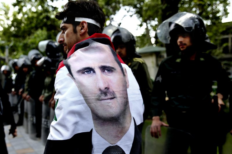 A Syrian man wrapped in a Syrian flag bearing the portrait of President Bashar Assad walks past anti-riot police during an anti-Israeli demonstration in front of the United Nations office in Tehran, Iran, on Monday.
