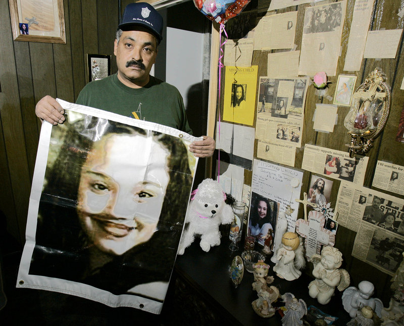 A 2004 photo shows Felix DeJesus, holding a banner showing his daughter’s photograph, standing by a memorial in his living room in Cleveland, Ohio.