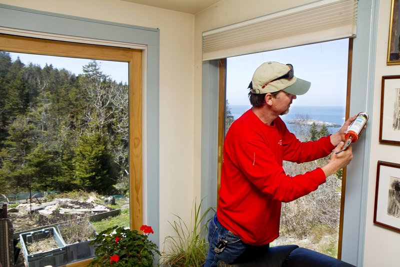 Scott Braley caulks a window frame to make a Monhegan Island home more energy efficient.