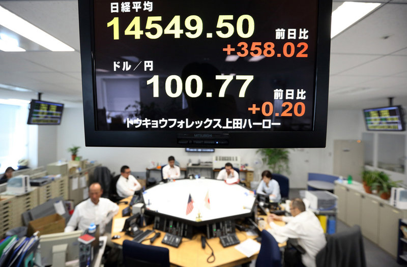 Dealers in Tokyo work under a monitor displaying a figure of the Nikkei 225 Stock Average, top, and the exchange rate of the yen against the U.S. dollar.