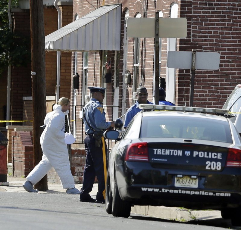 An investigator in protective clothing walks near the scene in Trenton, N.J., where a registered sex offender who held his girlfriend’s three children hostage was shot to death Sunday. Police rescued the children and recovered the bodies of their mother and a sibling.