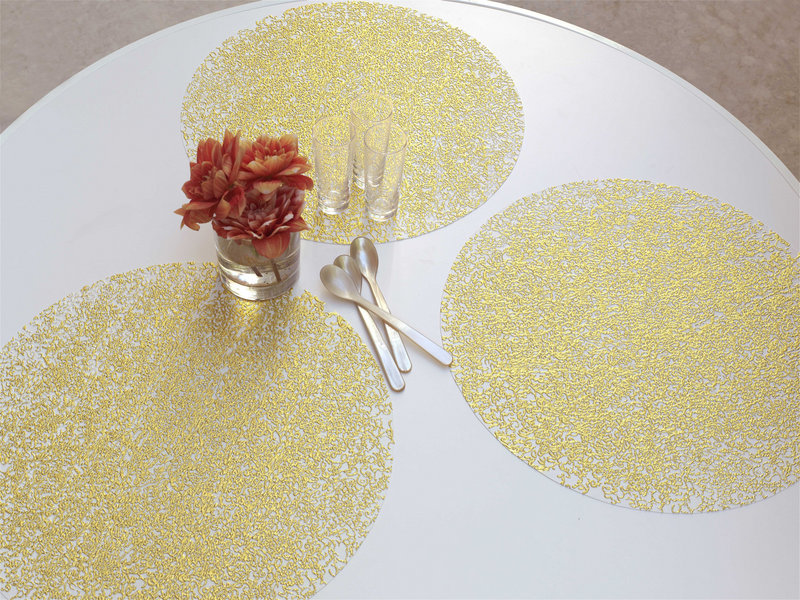 Pressed filigree gold-white placemats by Sandy Chilewich are spot printed with metallic foil to suggest the weathered look of a delicate old textile.