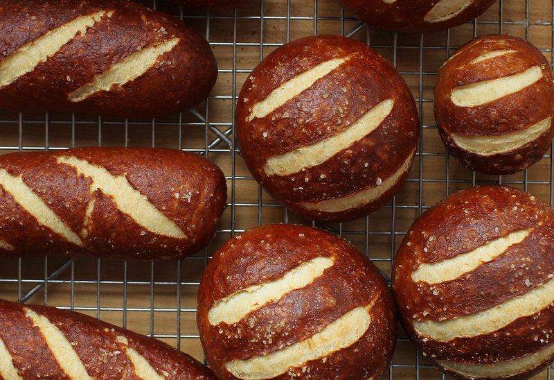 For pretzel bread, the rounds of dough are dipped in a baking soda bath, brushed with egg white, and sliced across the top with a box cutter or sharp knife before baking.