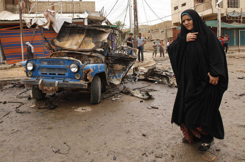 An Iraqi woman passes by the scene of a car bomb attack in a predominantly Shiite area of eastern Baghdad on Monday. A wave of car bombings across Baghdad’s Shiite neighborhoods and in the southern city of Basra killed dozens of people, police said.