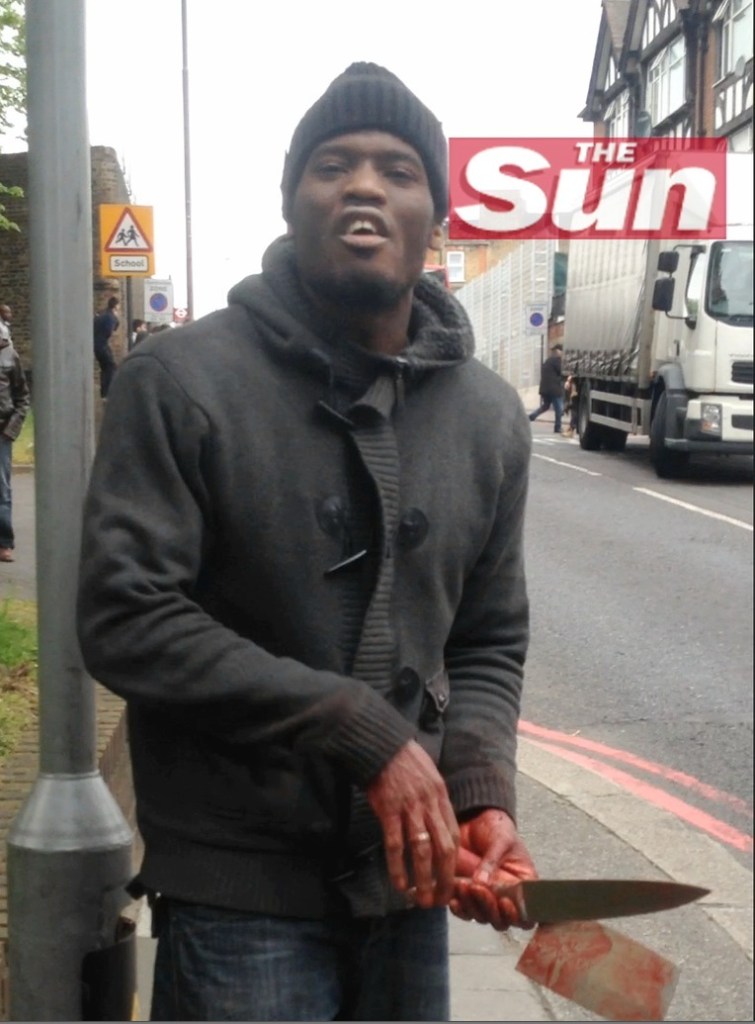 A possible suspect in the brutal, broad-daylight attack in London Wednesday holds bloodied weapons and appears to speak toward the camera, in this image from video made available by The Sun newspaper.