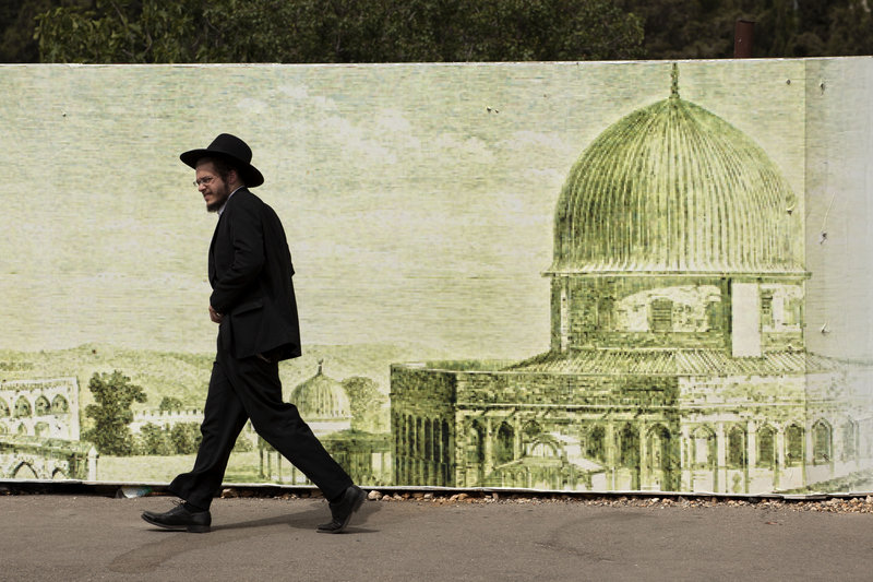Ultra-Orthodox Jews, like this man walking past a sign depicting the Dome of the Rock Mosque in Jerusalem, are among the most vocal opponents of a plan that would gradually limit what have been automatic exemptions from military service.