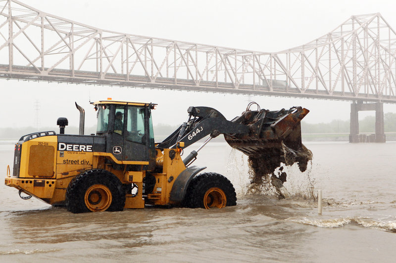 A worker clears mud and debris from a flooded street near the Martin Luther King Bridge in St. Louis in early May as flooding has been a problem all spring.