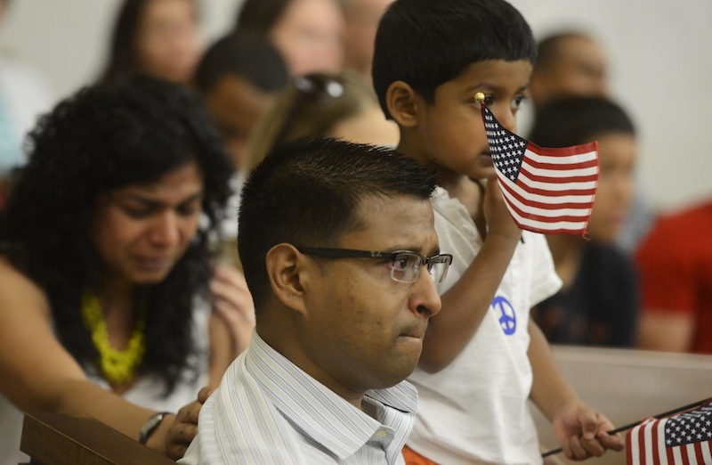 Vrushali Deshmukh, left, and Ash Ingole, center, newly naturalized citizens from India, get choked up while listening to "God Bless America" as Neil Ingole, 2, waves American flags during the naturalization ceremony at the York County Administrative Center on Thursday.