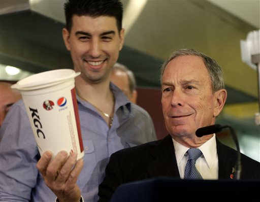 In this March 12, 2013, New York City Mayor Michael Bloomberg looks at a 64-ounce cup, as Lucky's Cafe owner Greg Anagnostopoulos, left, stands behind him, during a news conference at the cafe in New York. The mayors of New York, Los Angeles, Chicago and 15 other cities are reviving a push against letting government food vouchers be used to buy soda and other sugary drinks.