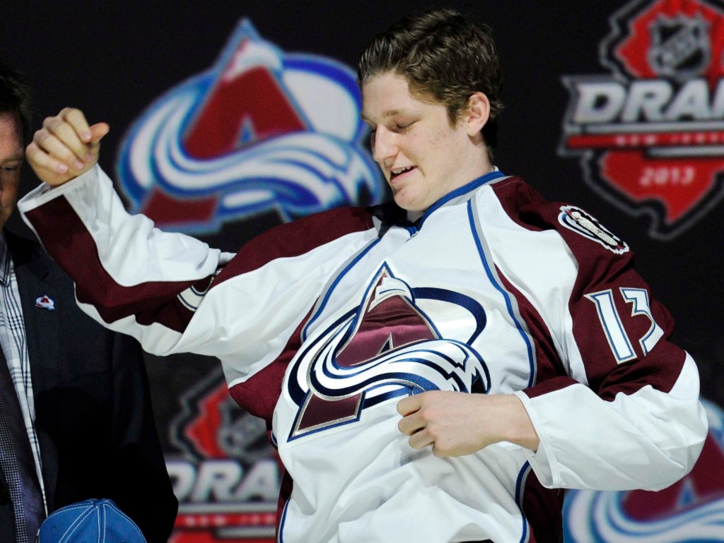 Nathan MacKinnon, a center, pulls on a Colorado Avalanche sweater after being chosen 1st overall in the first round of the NHL draft on Sunday.