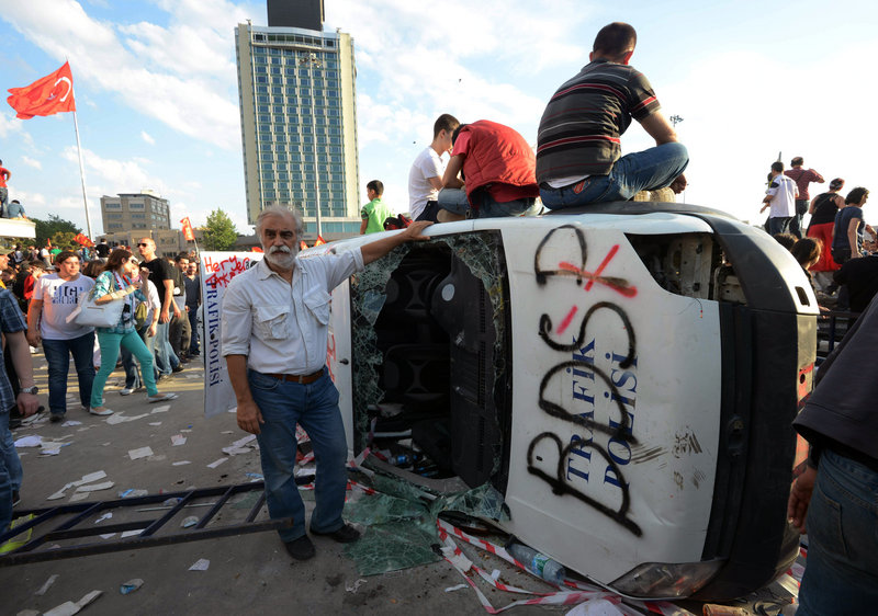 Turkish protesters climb onto a destroyed car Saturday at Istanbul’s Taksim Square. Police retreated from the square, removing barricades and allowing in thousands of protesters.