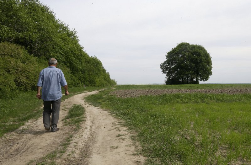 In photo taken May 10, Ivan Hrushka, 69, approaches the site of a peasant house – under trees in the distance on the right – where 21 people, including nine children, were burned alive on Dec.3, 1943, in his home village of Pidhaitsi close to Ukraine’s western city of Lutsk.