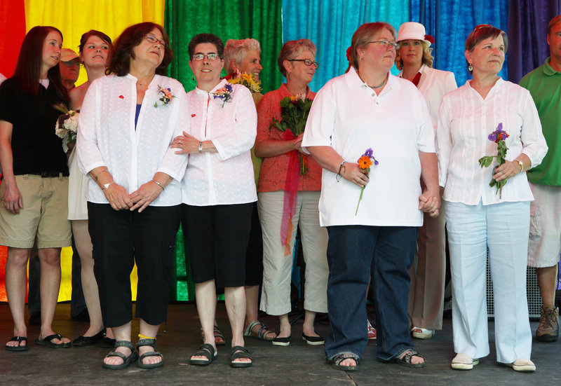Rose Larkin, left to right, and Deb DeTuccio, joined by Chris Andre and Chris Fleuriel, right, listen to the officiant during a mass wedding Saturday at Deering Oaks in Portland as part of the 27th annual Southern Maine Gay Pride Parade and Festival.