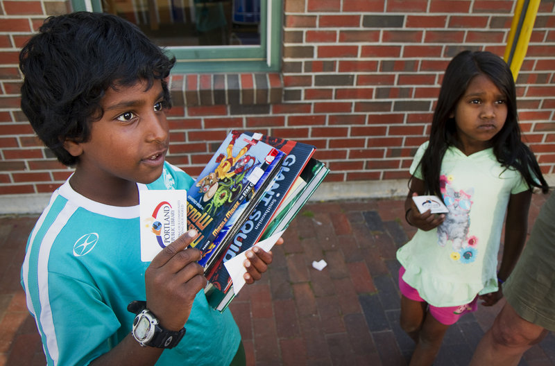 Toby Picher, 9, with an arm-full of books, and sister Cora, 6, show off their first library cards obtained from the Portland Public Library's mobile unit outside The Root Cellar on Washington Avenue on Friday, June 21, 2013. Students and parents can access books from the mobile unit, which will make regular visits around Portland throughout the summer vacation.