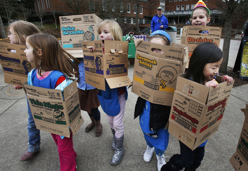 Wrapped in boxes emptied from earlier cookie sales, Girl Scouts from Troop 20337 in Eugene, Ore., fan out on the University of Oregon campus in search of more cookie customers. One year after the organization celebrated its 100th anniversary, even the proceeds of cookie sales are being questioned as to what they support.