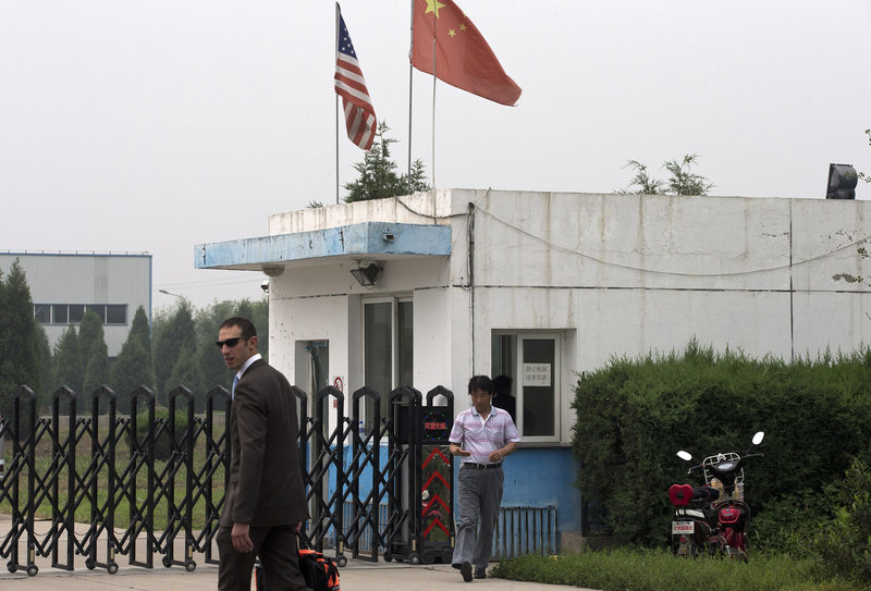 A U.S. Embassy employee and a Chinese official walk outside the closed gate at a plant where an American was being held.
