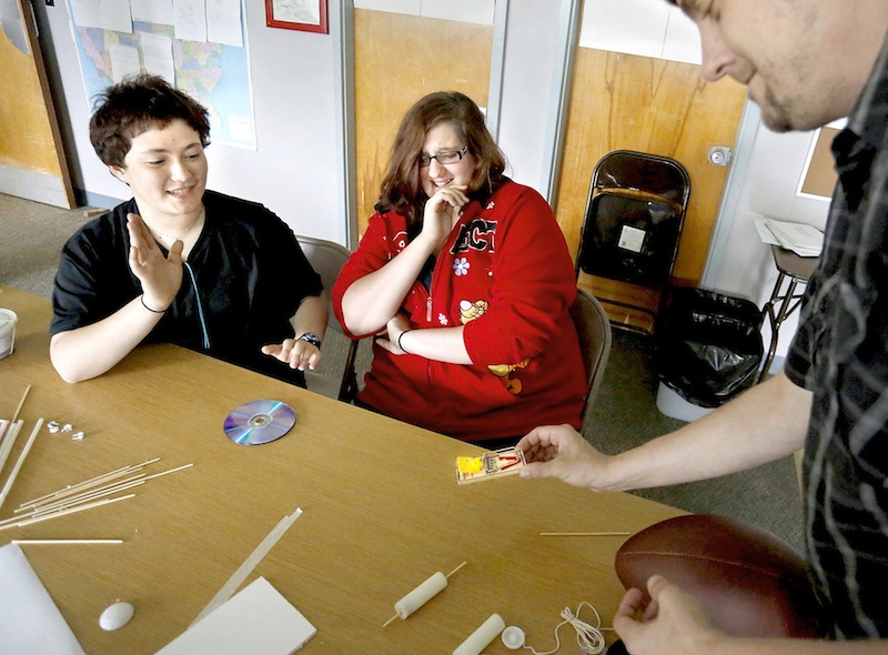 Caitlyn Harrison, 16, from Windham High School, left, and Tiffany Anderson, 16, from Windham High School, react as David West, an Americorps science teacher, places a set mousetrap on the table right before the trap went off while helping them build a mousetrap car at the Real School on Mackworth Island in Falmouth on July 10, 2013. A group of 16 girls are wrapping up a free, three-week STEM (science, technology, engineering, math) program, working with local companies to solve “real world” problems.