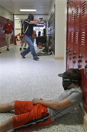In this July 11, 2013, photo, a Clarksville schools faculty member, wearing a protective mask, rear center, carries a practice handgun toward a classroom in the city's high school, as students portray victims in a mock school shooting scenario.