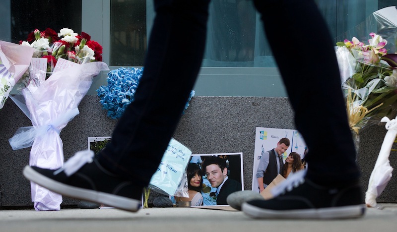 A pedestrian walks past photographs and flowers placed at a memorial for Canadian actor Cory Monteith outside the Fairmont Pacific Rim Hotel in Vancouver, British Columbia on Monday, July 15, 2013. Monteith, 31, was found dead in his room at the hotel on Saturday, according to police, who have ruled out foul play. (AP Photo/The Canadian Press, Darryl Dyck) CANADA;CANADIAN;BRITISH COLUMBIA;B.C.;VANCOUVER;CPPIXBC;CPPIXVANCOUVER;CPPIXBRITISHCOLUMBIA