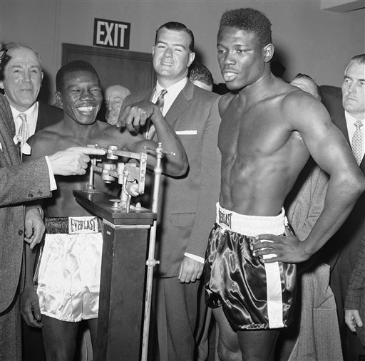 In this March 24, 1962, photo, welterweight champion Benny Paret, in white trunks, reads the weight of challenger and former champion Emile Griffith during the weigh-in for their title fight in New York. In center is James A. Farley, Jr., a member of the New York State Athletic Commission.