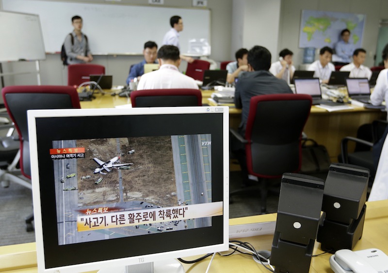 A screen showing a news program reporting about Asiana Airlines flight 214 which took off from Seoul and crashed while landing at San Francisco International Airport as employees of Asiana Airlines work at Crisis Management Center of Asiana Airlines head office in Seoul, South Korea, Sunday, July 7, 2013. (AP Photo/Lee Jin-man, Pool)