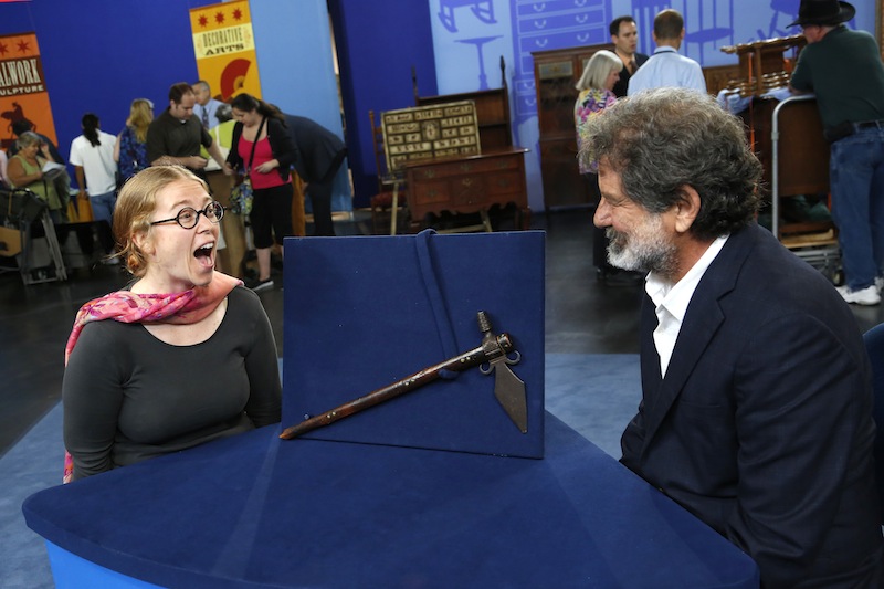 This June 22, 2013 photo released by PBS shows Ted Trotta, of Trotta-Bono, Ltd., right, looking at Lisa as she reacts about information about her Spontoon Tomahawk Pipe during the taping of the popular appraisal show "Antiques Roadshow," in Anaheim, Calif. Top-rated PBS series "Antiques Roadshow" is on the move, taping programs in eight U.S. cities for its upcoming 18th season. (AP Photo/PBS)