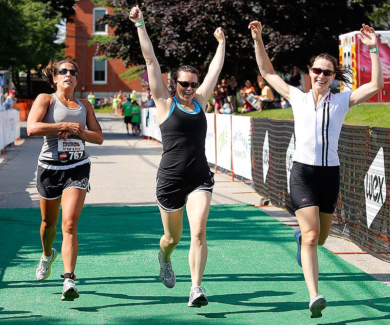 TriStrength team member Faye Maier of Scarborough stops the clock on her watch as teammates Kiely Foley of South Portland and Ellen Janokowski of Portland, right, celebrate their first-place finish in the survivors team competition Sunday in the Tri for a Cure in South Portland.