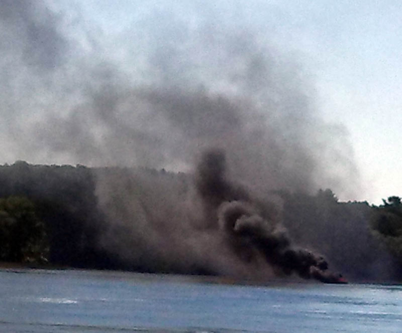 A burning motor boat drifts south on the Kennebec River, before running aground in Pittston on Friday.