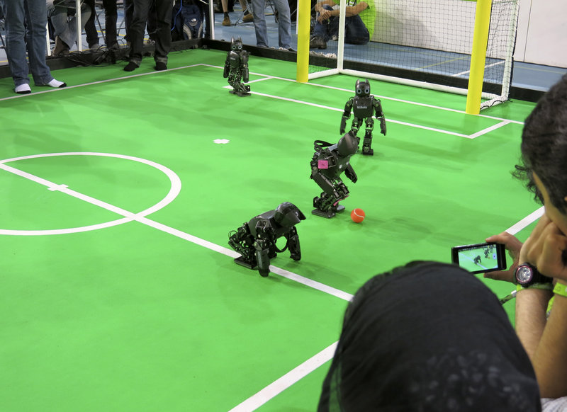 Robots in the "kids" humanoid division compete during the RoboCup championships in Eindhoven, Netherlands. The robot in the foreground is standing back up again after a fall. One of the competition's goals is to foster new technology for non-soccer uses.