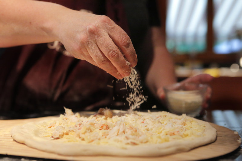 Jill Strauss sprinkles Parmesan cheese on the pie, which also is topped with bechamel sauce, crab meat and cheddar.