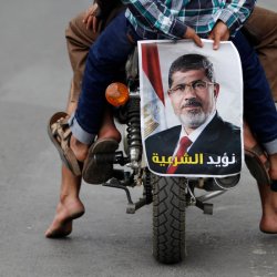 A pro-democracy protester holds a photo of deposed Egyptian President Mohamed Mursi while riding a motorcycle during a demonstration against what they said was a military coup against Mursi, in Sanaa
