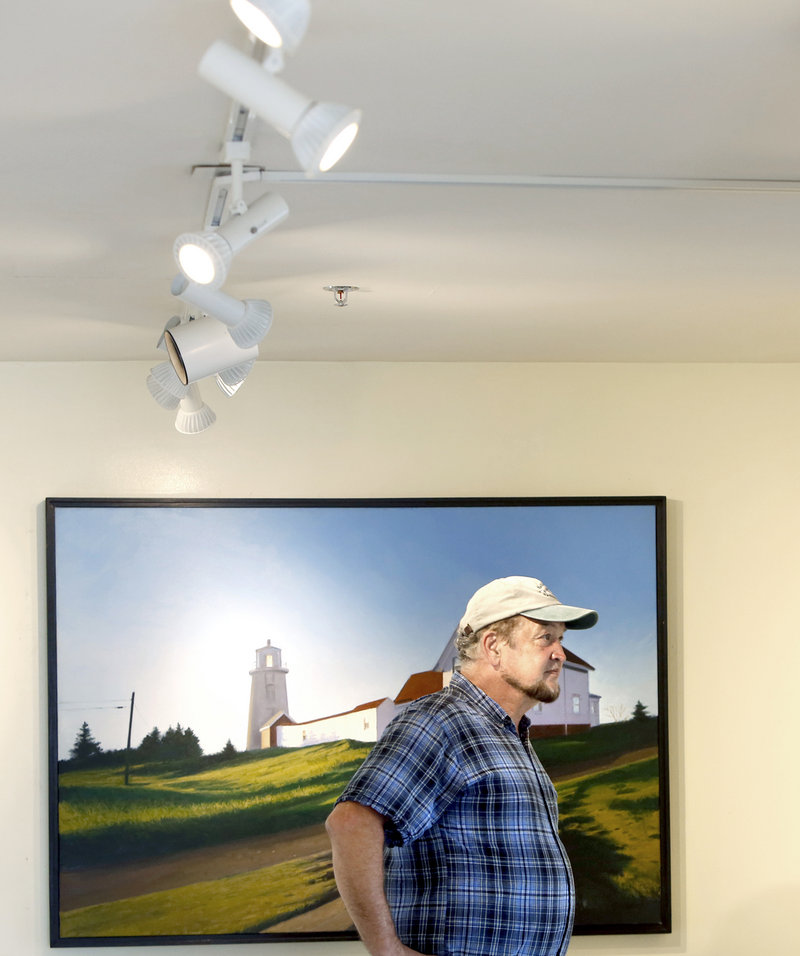 Michael Mayhew of Heliotropic Technologies looks over paintings at Gleason Fine Art in Boothbay Harbor. His company installed high-efficiency light bulbs at Gleason Fine Art and other businesses to reduce energy use.