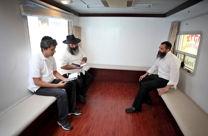 Volunteer Abraham Rosen, center, reads next to Ronen Corcie, left, and volunteer Adan Ogen inside the mitzvah tank. The vehicles seek to engage people who might be avoiding religion.