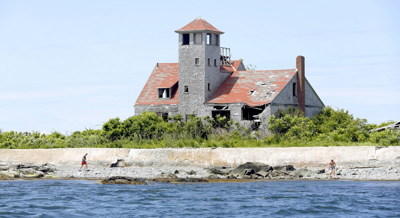 Roger Troudeau of Belgium, left, walks on Wood Island with his daughter Kate. The Wood Island Life Saving Station behind them was built in 1908 and staffed by civil servants who watched for ships in distress near Portsmouth Harbor.