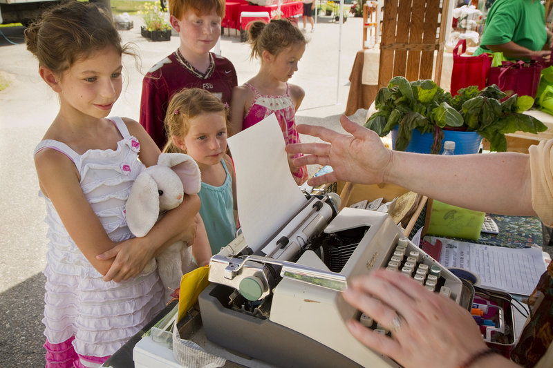 Abigail Kline, 9, of Destin, Fla., at left, watches with other children as organic farmer Holly Morrison of Pownal, loads up the typewriter to create a poem commissioned by the youngster at the Cumberland Farmer’s Market on Saturday.