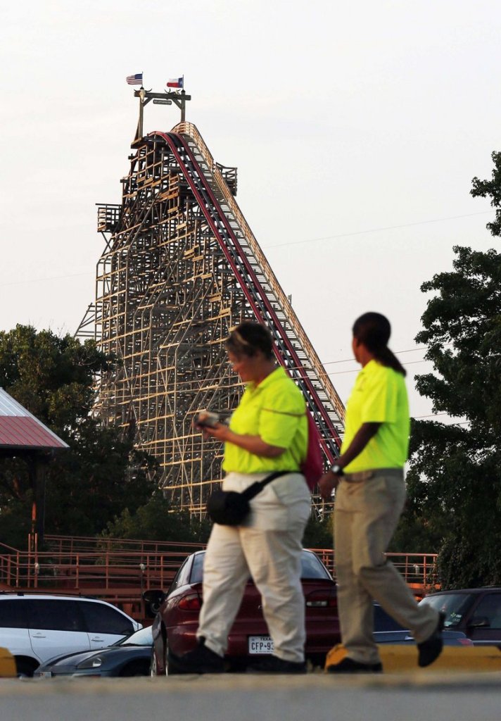 Six Flags Over Texas workers pass the Texas Giant roller coaster in Arlington, Texas, where a woman died Friday.
