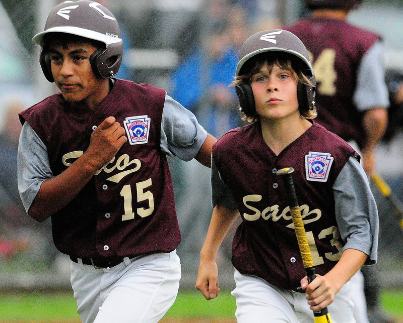 Anthony Bracamonte, left, and Timmy Smith head back the Saco dugout after scoring on Luke Chessie’s single in the fourth inning against Bayside.