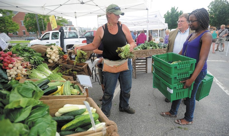 Hanne Teirney of Cornerstone and Fail Better Farms offers fresh organic produce to Noma Moyo, 21, a Colby College junior, and Joe Klaus, food services manager at Colby College, at the Waterville Farmers Market on Thursday.