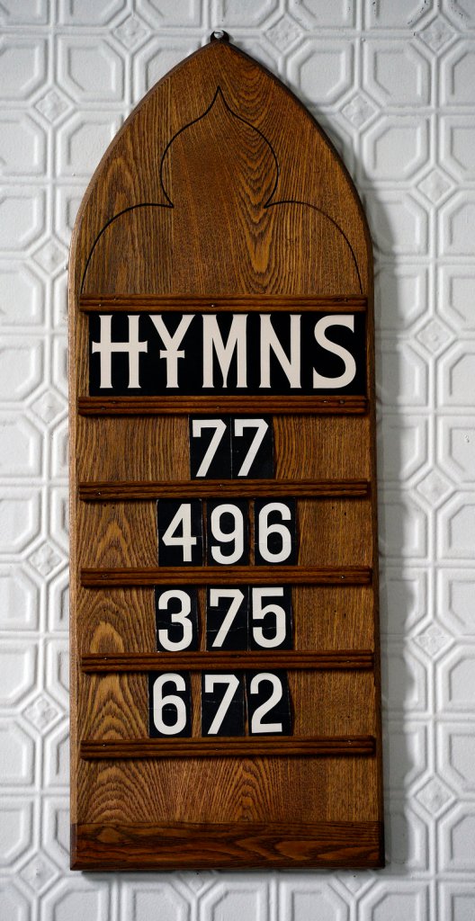 A board lists the hymns for the Sunday service.