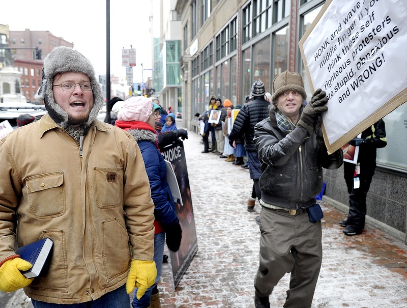 Portland businessman Mike Fink, right, passes anti-abortion Pastor Jeremy Hiltz of Chelsea during a counter-protest on Congress Street in Portland in January. Fink said Monday he is closing his nearby deli because of the effect of the weekly protests on his business.