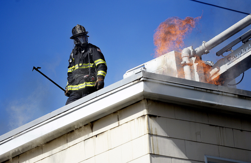 A firefighter pauses while working on the roof to keep an eye on flames at 129 Grant St. in Portland on Wednesday. A two-alarm fire heavily damaged the top story of the three-story apartment building.