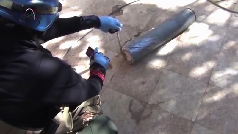 In this image taken from amateur video posted online, appearing to show a presumed UN staff member measuring and photographing a canister in the suburb of Moadamiyeh in Damascus, Syria, Monday Aug. 26, 2013, the suburb of Damascus where the Syrian regime allegedly used deadly chemical weapons. AP could not verify the authenticity of the video, but it is consistent with Associated Press reports. U.N. experts collected samples and testimony from Syrian doctors and victims of an alleged chemical weapons attack on Monday following a treacherous journey through government and rebel-held territory during which their convoy was struck by snipers. (AP Photo/MEDIA OFFICE OF MOADAMIYEH)