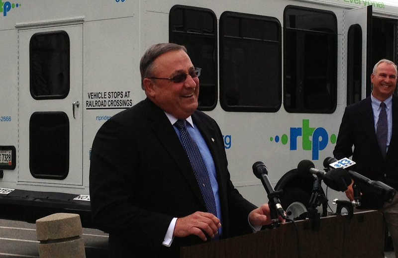 Gov. Paul LePage announces the launch of a bus refurbishing program designed to extend the life of regional transit buses run by nonprofit agencies. At right is Tim Corbett, executive director of the Maine Military Authority, which is doing the overhauls. A refurbished bus run by the Portland-based Regional Transportation Program is at rear.