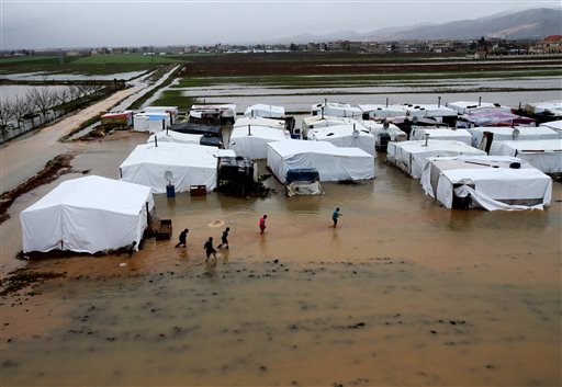In this Jan. 8, 2013, photo, Syrian refugees make their way in flooded water at a temporary refugee camp, in the eastern Lebanese town of Al-Faour near the border with Syria.