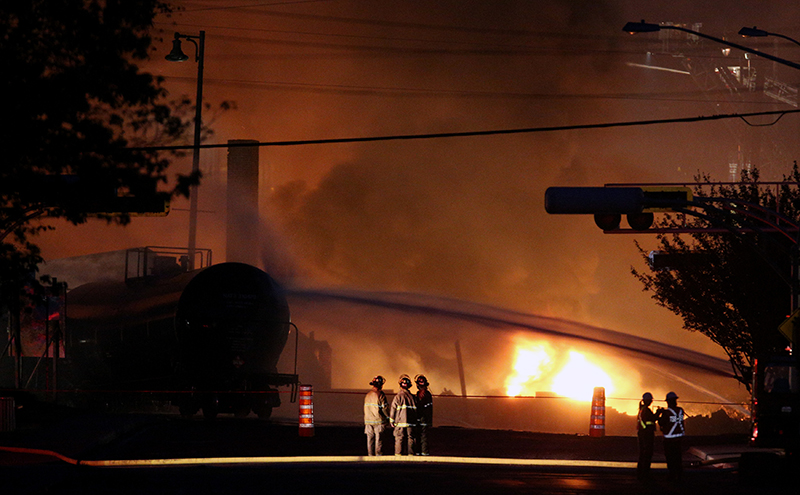 Firefighters look at a train wagon on fire at Lac Megantic, Quebec, July 6, 2013 after a runaway oil train crashed and caused numerous explosions. 47 people died and much of the Quebec town was destroyed. The company faces over $200 million in crash claims but only has a $25 million policy.(REUTERS/Mathieu Belanger)