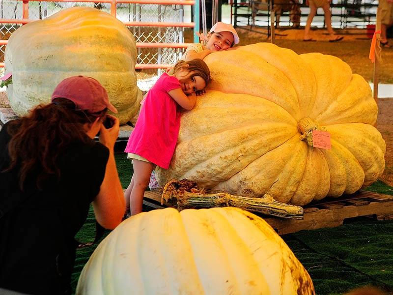 Alane Kennedy, left, photographs her daughters, Savannah Myers, 3, and Leilani Myers, 7, all of St. George, as they pose among the giant pumpkins and squash on the opening day of the 2013 Windsor Fair today in Windsor. The fair runs through Labor Day and the fairgrounds are located on Route 32, between Routes 17 and 105.